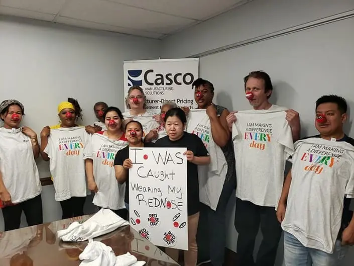 A group of people wearing red noses. One of them is holding a sign that says "I was caught wearing my red nose". The rest of them are holding t-shirts that say "I am making a difference every day".