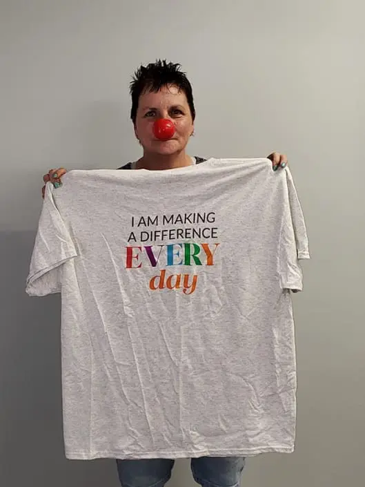 A woman wearing a red nose and holding a shirt that says "I am making a difference every day"
