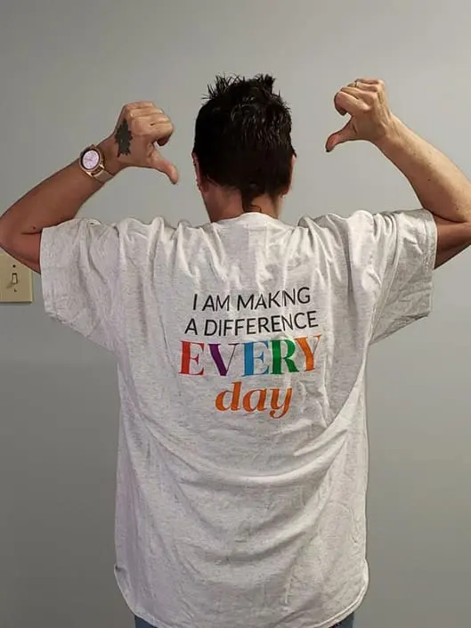 A woman pointing to the words on her tshirt, which reads "I am making a difference every day".