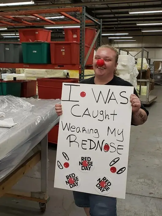 A woman wearing a red nose. She is holding a sign that says "I was caught wearing my red nose".
