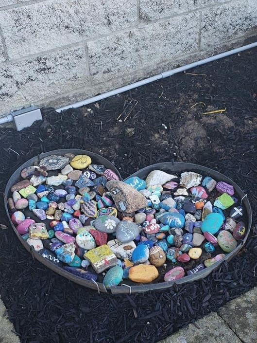 A heart-shaped bowl filled with colorful painted rocks.
