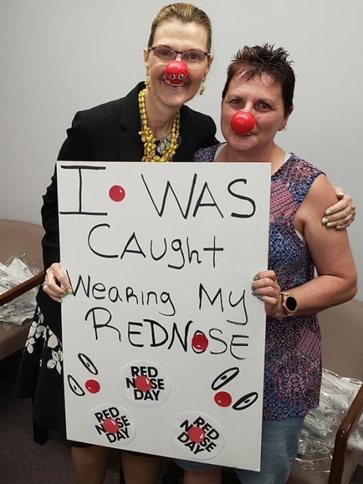 Melissa Mangold (CEO of Casco) and Liz Boyer (Casco Employee). They are wearing red noses and holding a sign that says "I was caught wearing my red nose".