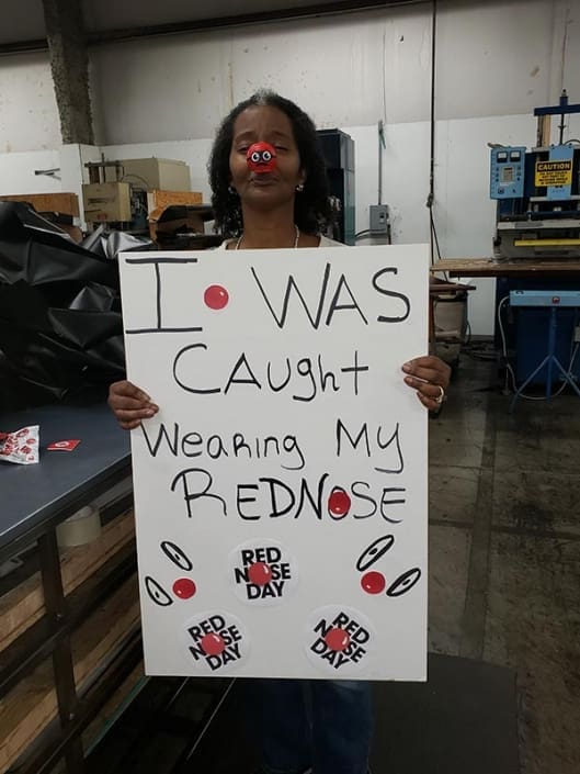 A woman wearing a red nose. She is holding a sign that says "I was caught wearing my red nose".
